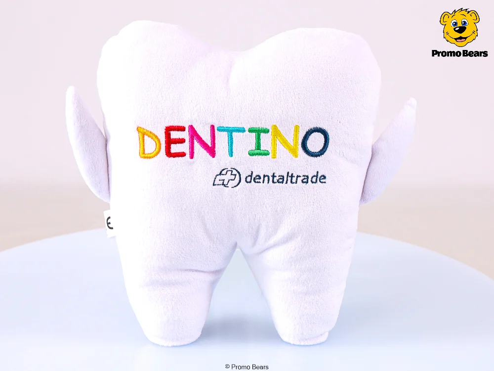 Soft white plush tooth toy with 'DENTINO' in rainbow letters and the 'dentaltrade' logo.